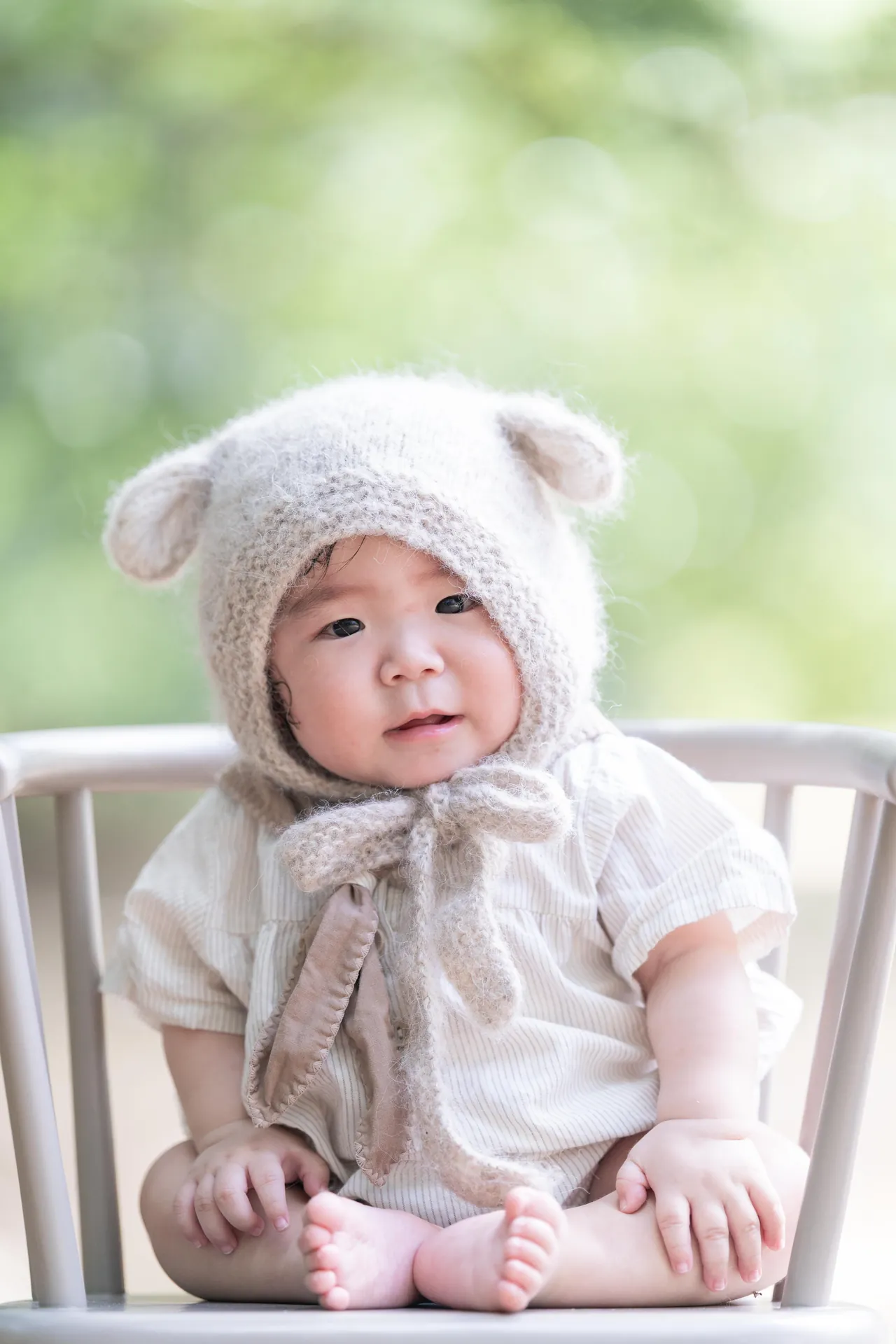 くまの耳の帽子をかぶって座る赤ちゃんの写真
