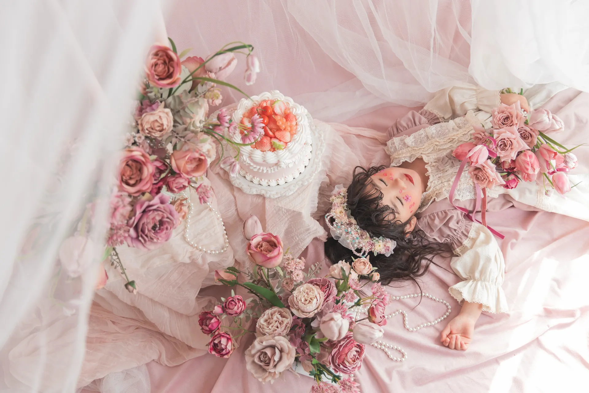 ピンクのバラとケーキに囲まれて寝転ぶ女の子の写真