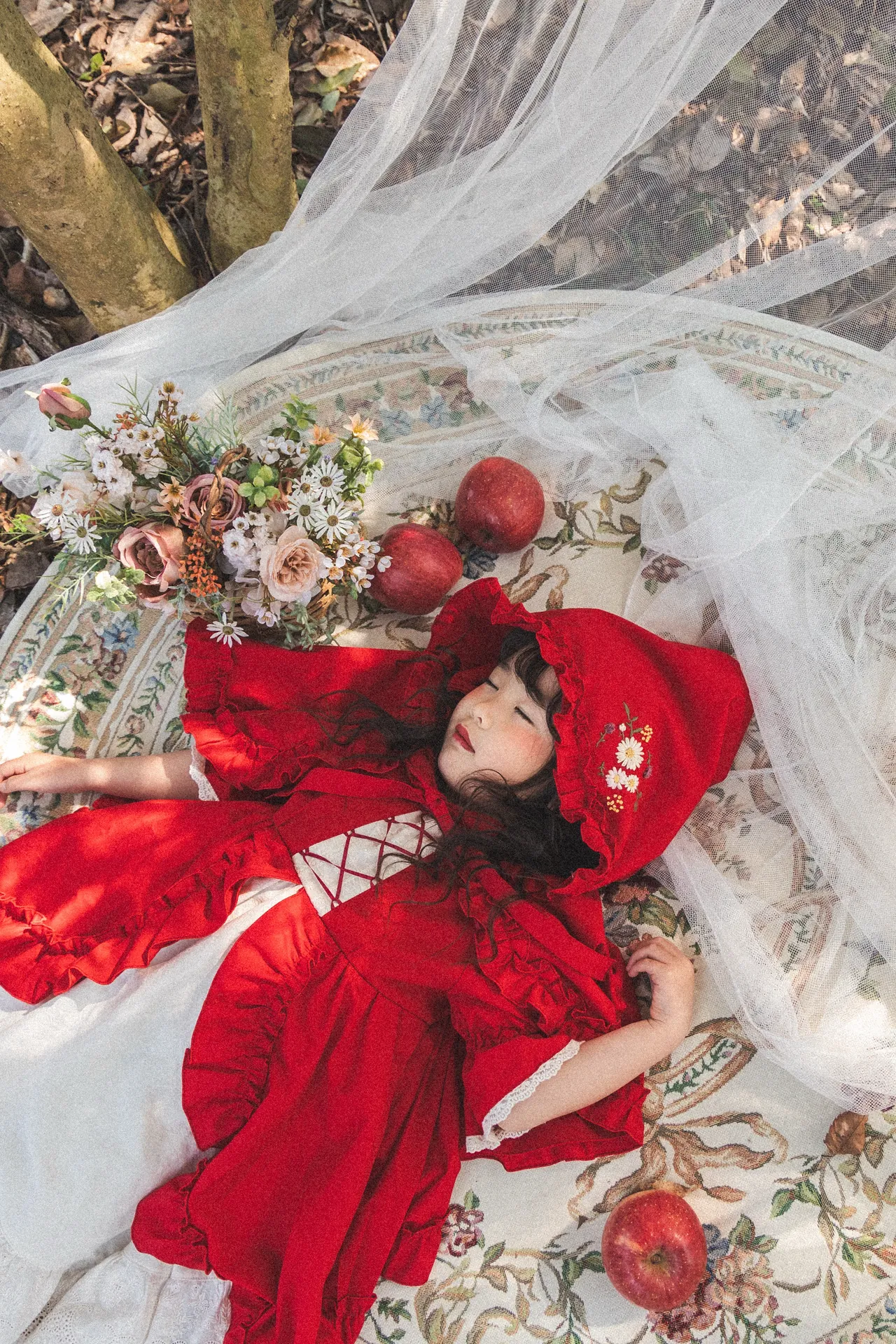 赤ずきんの衣装で、りんごと花に囲まれて眠る女の子の写真