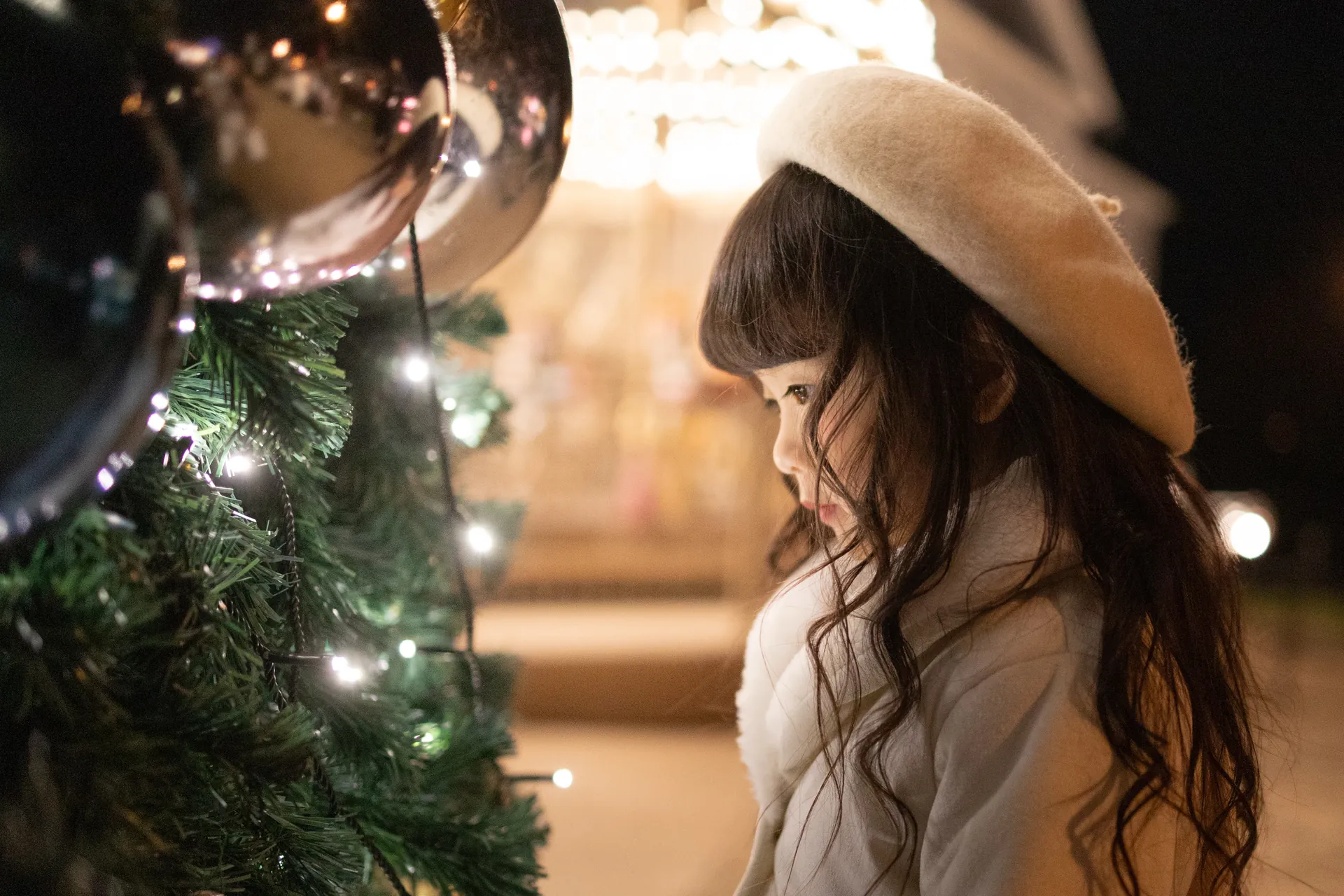 イルミネーションの前で、ベレー帽の女の子が横を向いている写真