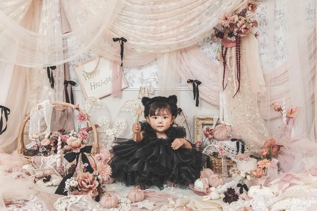 ハロウィンの飾りのセットで、黒いドレスの女の子が座っている写真