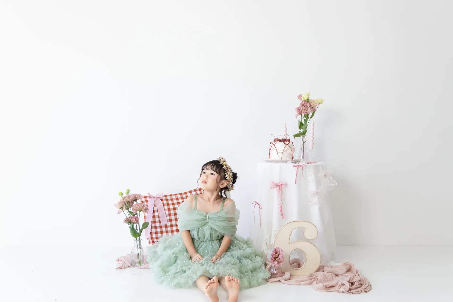 白い背景のセットで、グリーンのドレスの女の子と「6」の飾りの写真