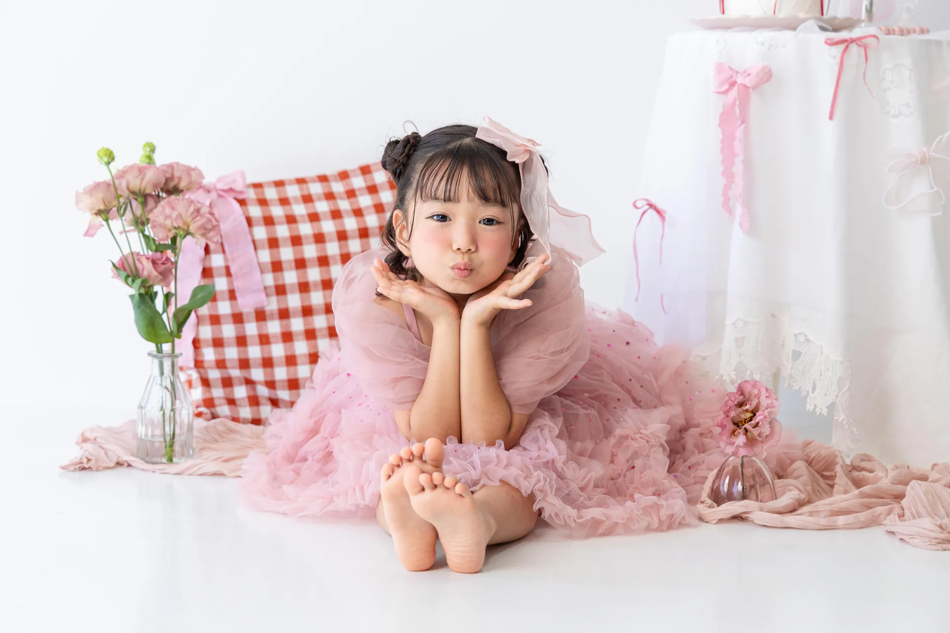 赤いギンガムチェックのクッションの前で、ピンクのドレスの女の子が頬杖をついている写真